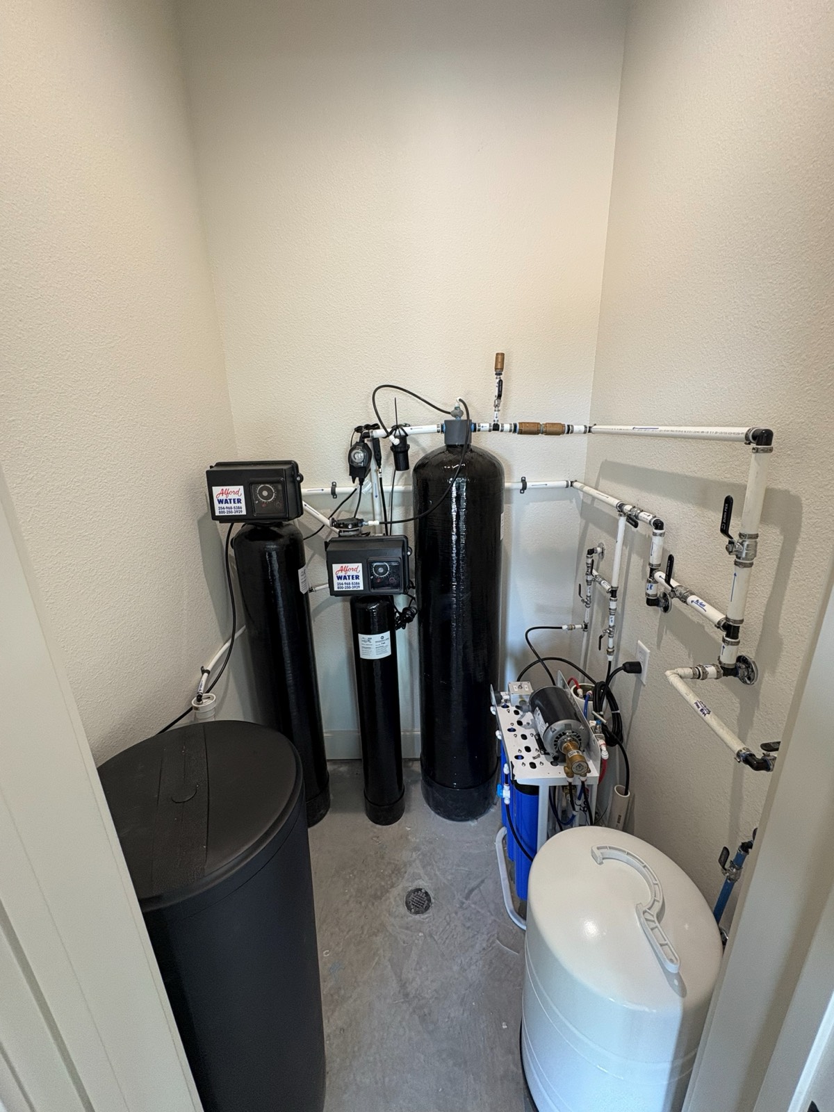 Residential water softener and reverse osmosis system installed in a utility closet.